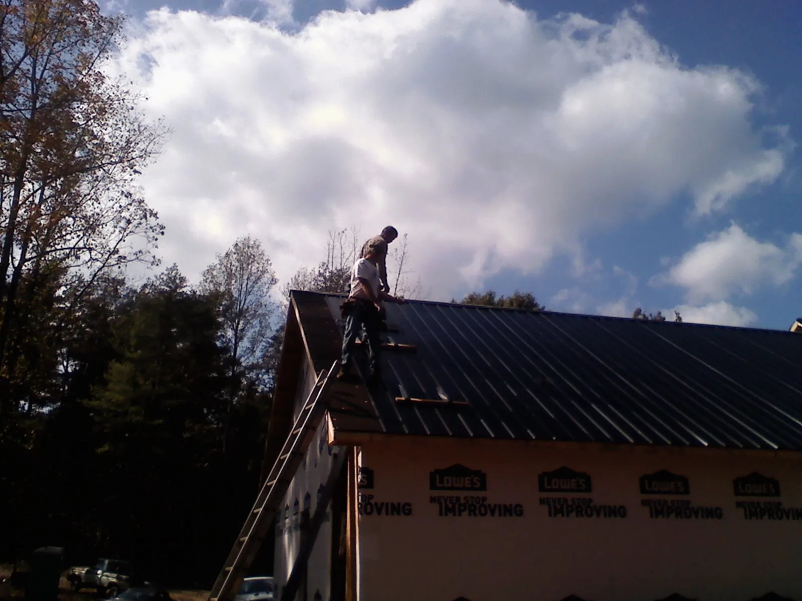 Roofer fastening dark metal panels high against a cloudy sky, from a Roof Inspection job in Gonzales