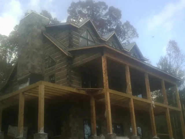 Stone chimney and dormers on a large log home with a timber porch in Gonzales