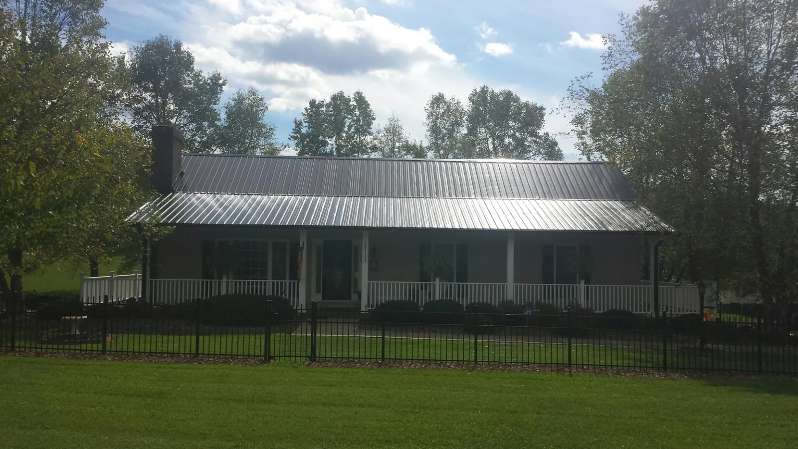 Gray metal roof on a brick ranch with a full width front porch — Gutter Guard Installation work by our crew in Gonzales