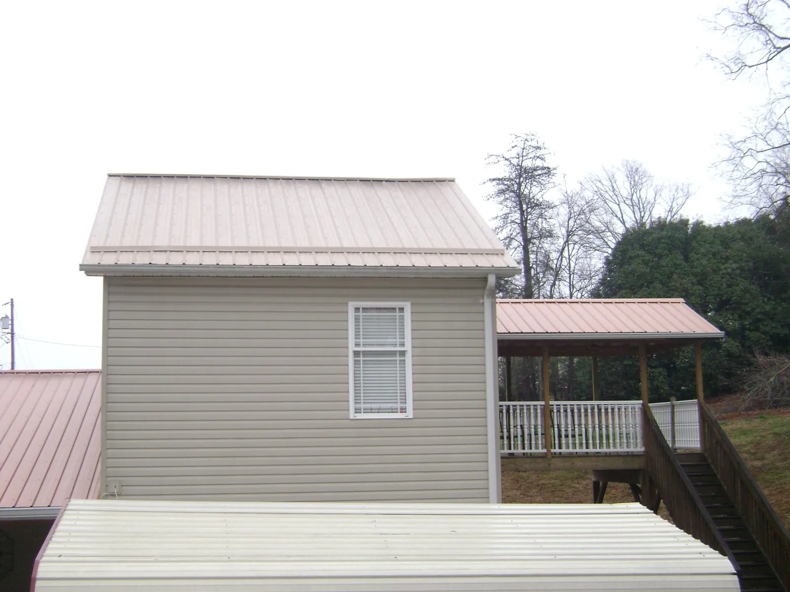 Tan metal roofs on a two story addition and attached porch, from a Roof Replacement job in Gonzales